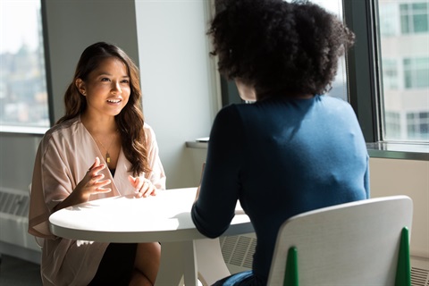 Two women sit at a table and talk