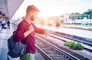 A man checks the time on his watch while waiting at a train station.