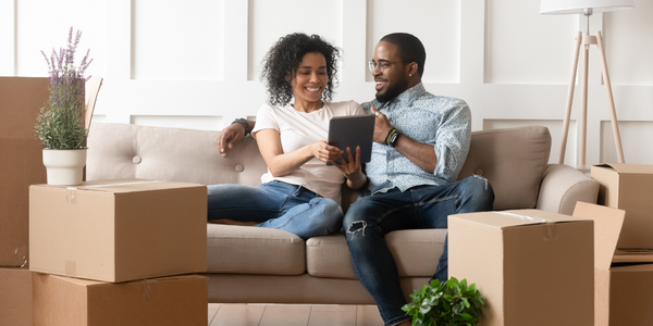 A couple sits on a couch surrounded by boxes